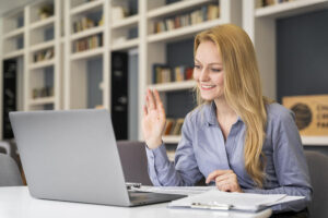 Frau winkt Kollegen in Remote-Work-Meeting über das Notebook zu.