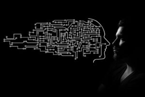 Künstliche Intelligenz und Mensch: Dem Foto eines männlichen Gesichts wird eine gezeichneter Kopf gefüllt mit technischen Schaltungen gegenübergestellt.